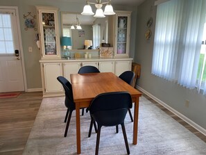 Un comedor con una mesa y sillas de madera, una cocina al fondo y una ventana con persianas.