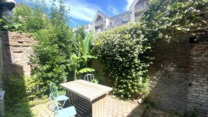 A courtyard with a wooden table and chairs, surrounded by brick walls and greenery.