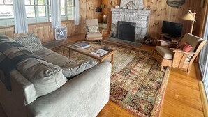 A cozy cabin interior with a stone fireplace, wooden walls, a sofa, and a television. - Waterfront on Sebago Lake (STANDISH)