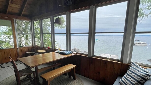 A wooden cabin with a dining table and benches, large windows with a view of the water, and a blue sofa with striped pillows. - Waterfront on Sebago Lake (STANDISH)