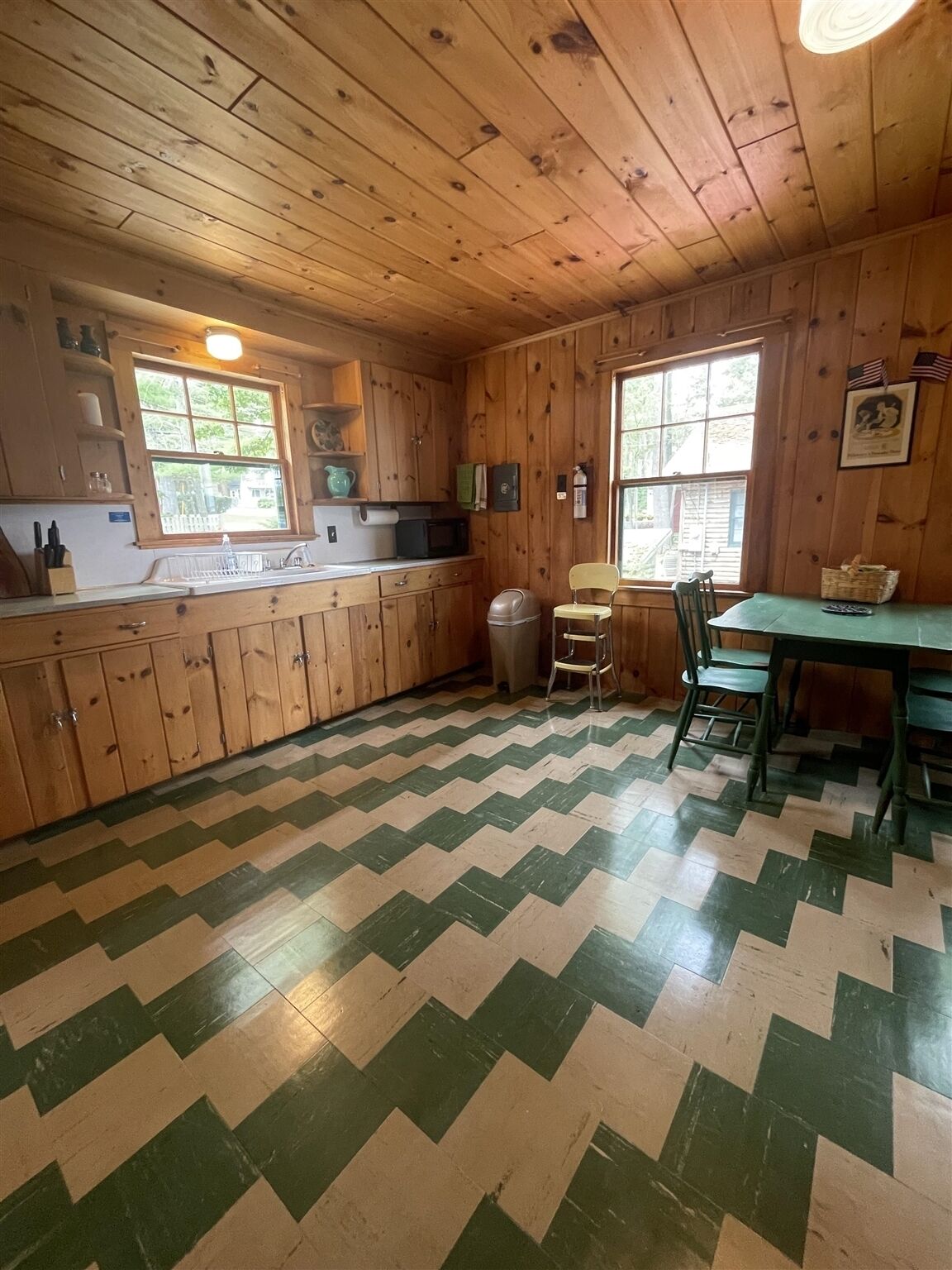 Interior de una cabaña de madera con cocina, que incluye un ventanal grande, una zona de comedor con mesa y sillas, y un suelo con diseño.