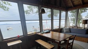 A cozy cabin with a wooden interior, a dining table with benches, a large window overlooking a lake with boats, and a view of the water. - Waterfront on Sebago Lake (STANDISH)