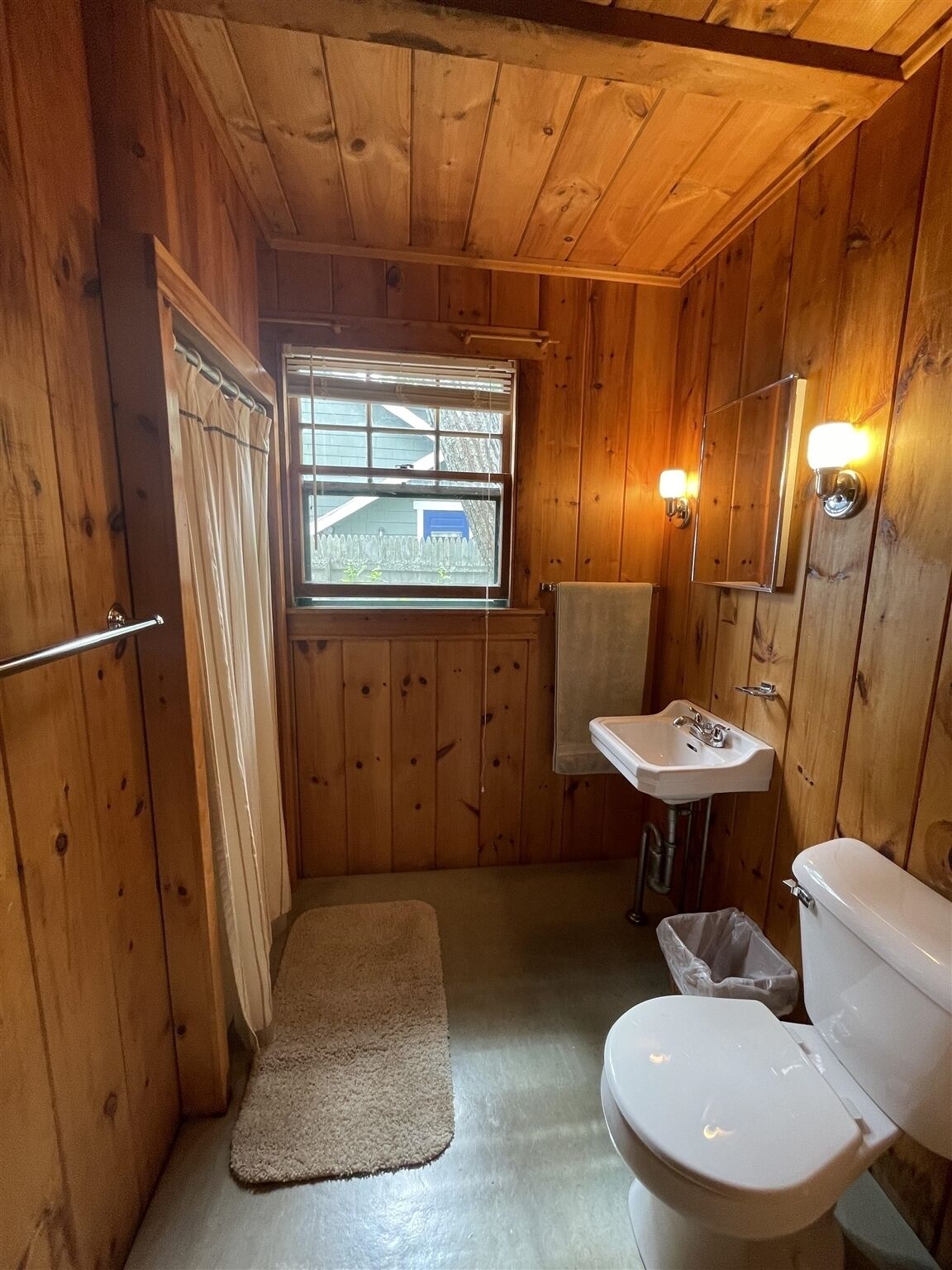 Un baño revestido de paneles de madera con ventana, un lavabo, un inodoro y un perchero para toallas.