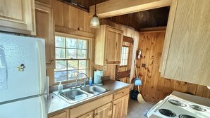 A rustic kitchen with wooden cabinets, a white refrigerator, a sink, and a stove.
