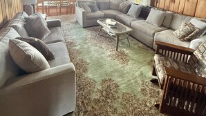 A cozy cabin interior with a large sectional sofa, a coffee table, and a rustic wooden ceiling.