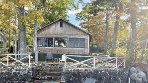 A rustic cabin with a stone wall and wooden deck, surrounded by trees.