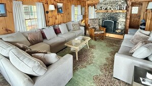 A cozy log cabin interior with a large sofa, a fireplace, and a stone wall.