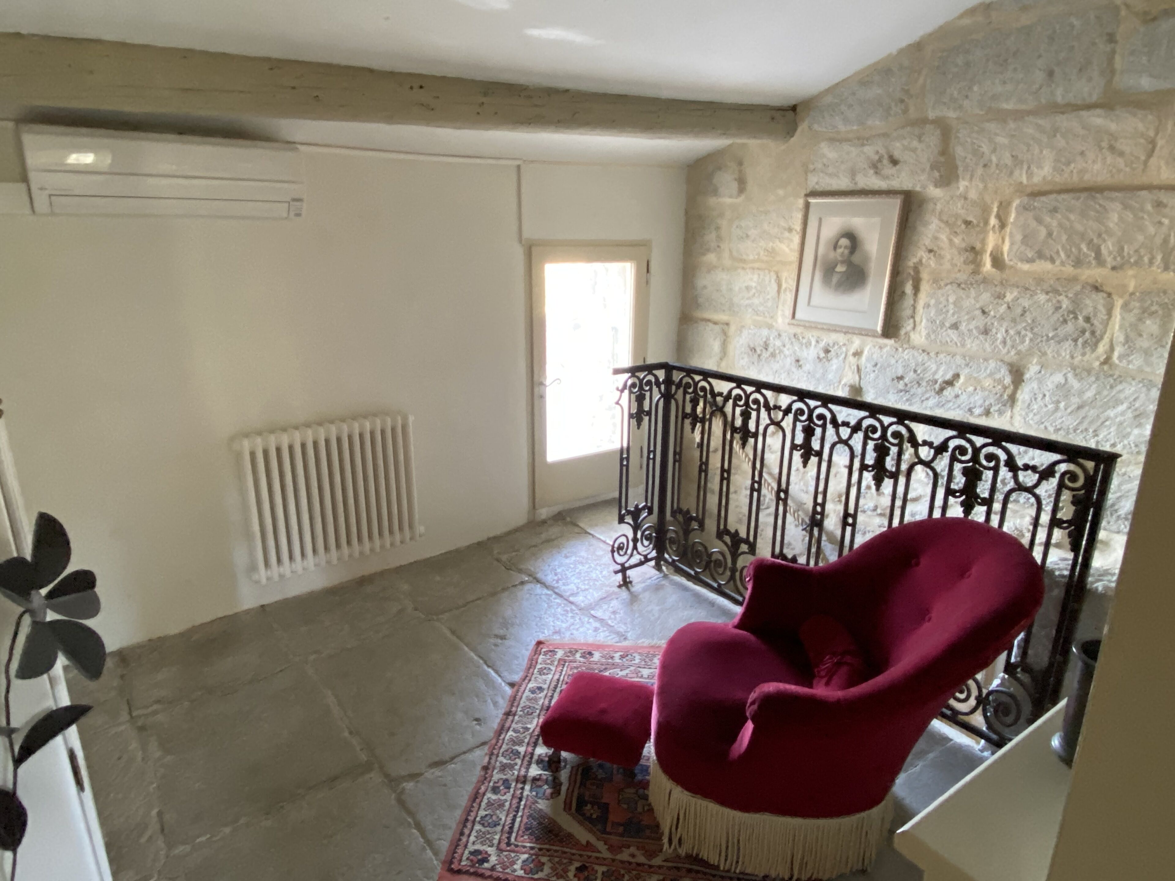 A room with a stone floor, a radiator, a window, a fireplace, and a red armchair.