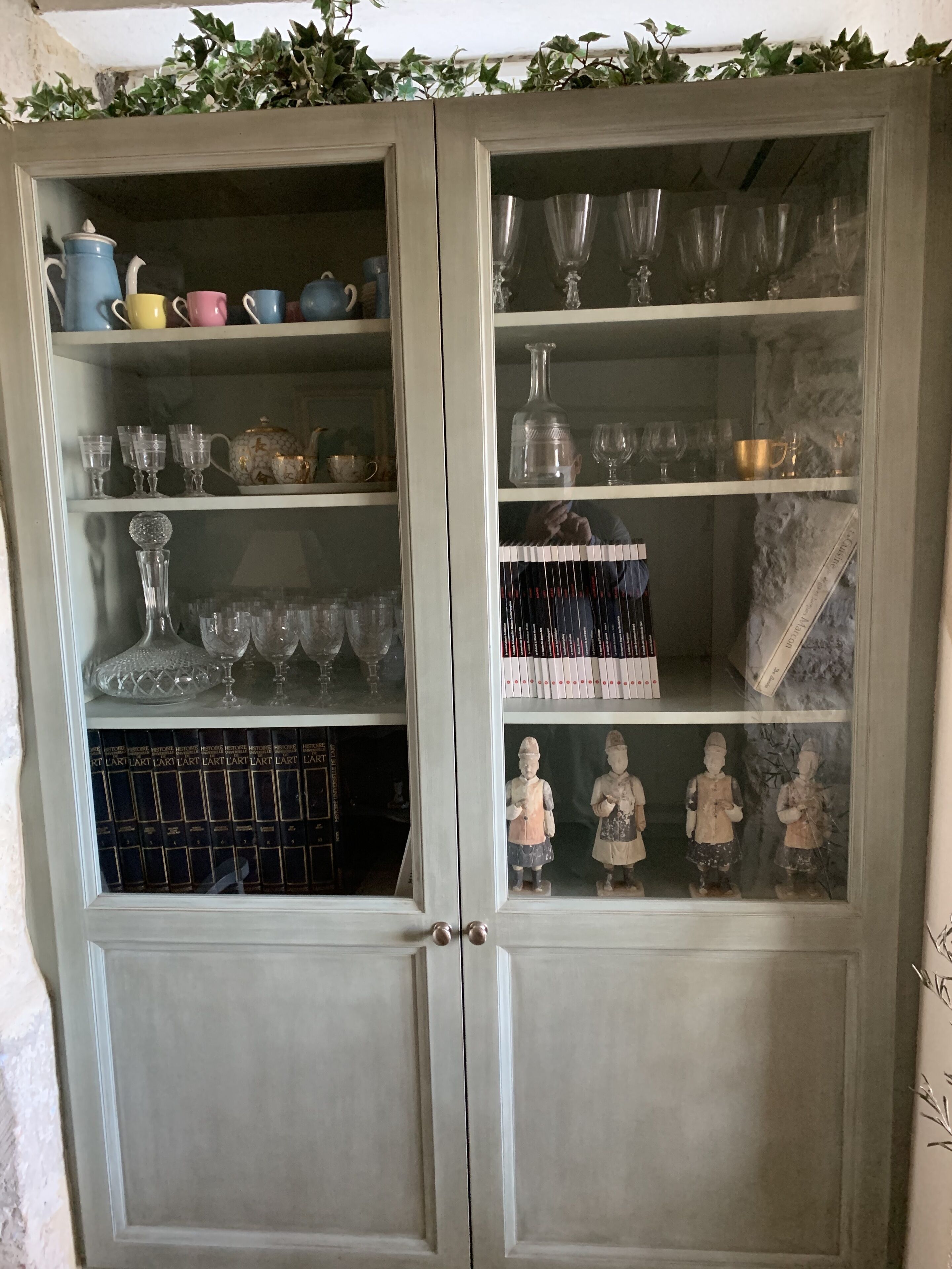 A cabinet with glass doors containing various glassware, books, and figurines.