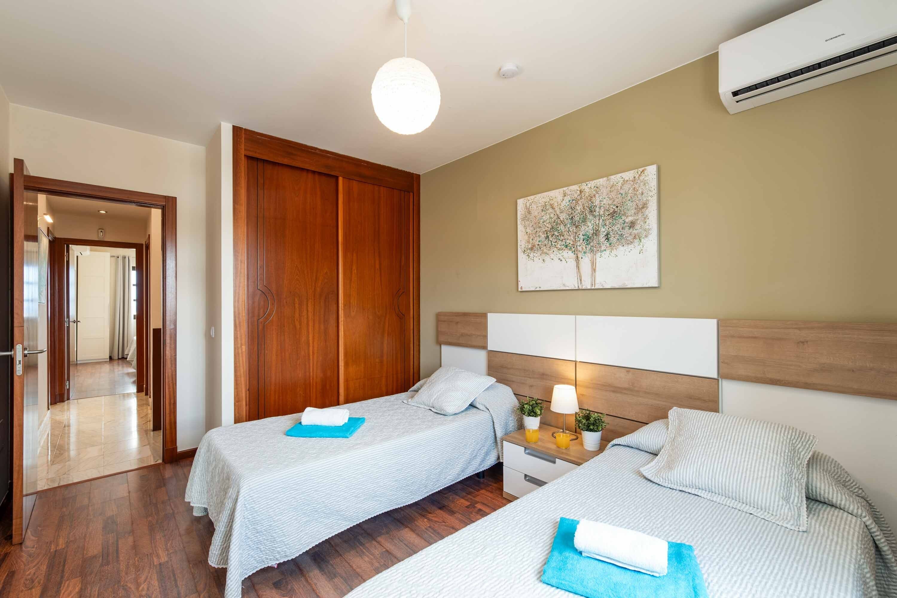 Une chambre d’hôtel avec deux lits, une armoire en bois, un appareil de climatisation et un tableau au mur.