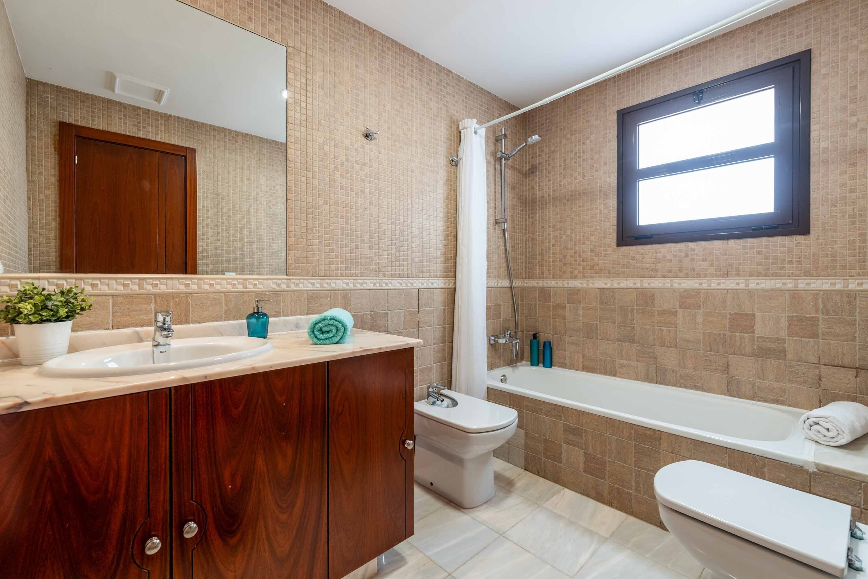 A bathroom with a wooden vanity, a sink, a bidet, a bathtub, and a window.