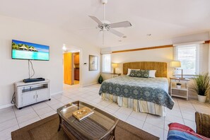 Una habitación de hotel con cama, televisión, ventilador de techo, una mesita y una silla.