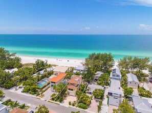 An aerial view of a coastal residential area with houses, a beach, and a clear blue ocean.