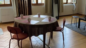 A room with a round table, four chairs, and large windows with curtains.