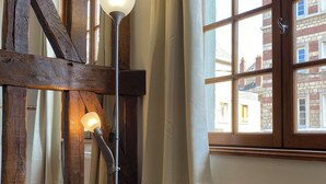 A room with exposed wooden beams, a floor lamp, a radiator, and a window with curtains.