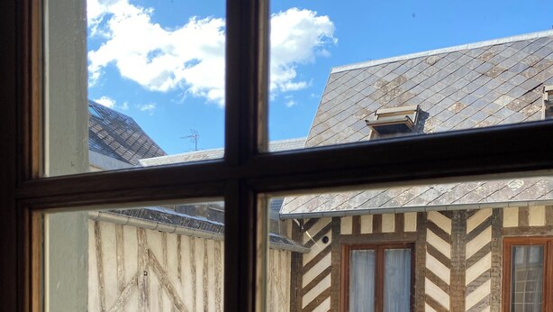 A view through a window of a traditional half-timbered building with a sloped roof and a visible chimney.