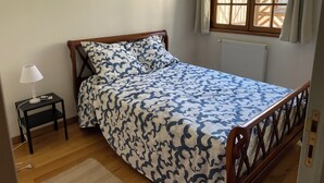 A bedroom with a bed, a nightstand, a lamp, a framed picture on the wall, and a window with curtains.