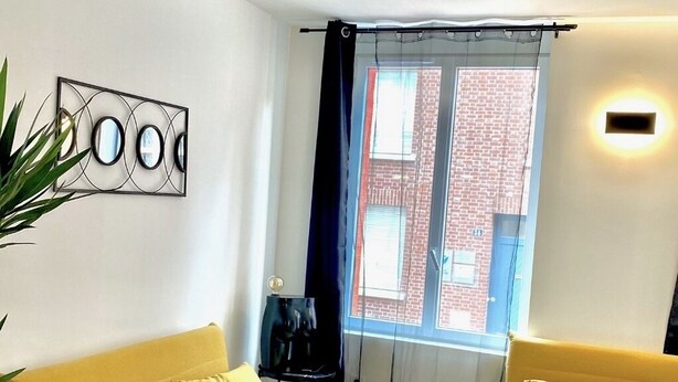 A modern living room with a yellow sofa, a glass coffee table, and a large window with curtains. - Appartement REZ DE Chaussee (Amiens)
