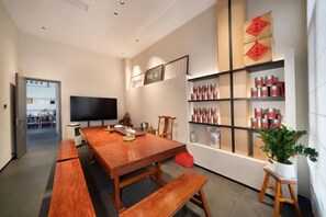 Un comedor moderno con una mesa de madera y bancos, un televisor de pantalla plana y un estante con objetos rojos y blancos.