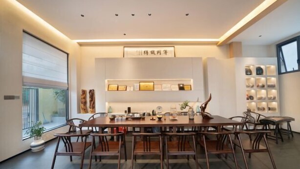 Un espace repas moderne avec une longue table en bois et des chaises, une étagère ornée de divers objets et une fenêtre offrant une belle vue.
