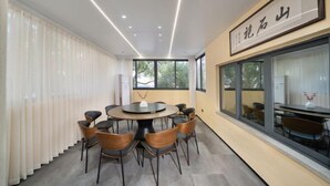 Un espace de salle à manger moderne avec une table ronde et des chaises, de grandes fenêtres et un plafond doté d’un éclairage linéaire.