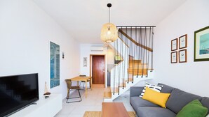 A modern living room with a flat-screen TV, a gray sofa with yellow and green cushions, a wooden coffee table, and a staircase with a wooden railing. - Hedera Estate, Hedera A16 (Dubrovnik)