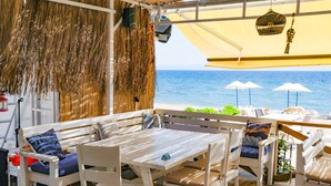 Un área de estar al aire libre con mobiliario blanco, una mesa y sombrillas con vistas al mar.
