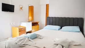 Una habitación de hotel con cama, televisión, mesita de noche de madera, escritorio y espejo.