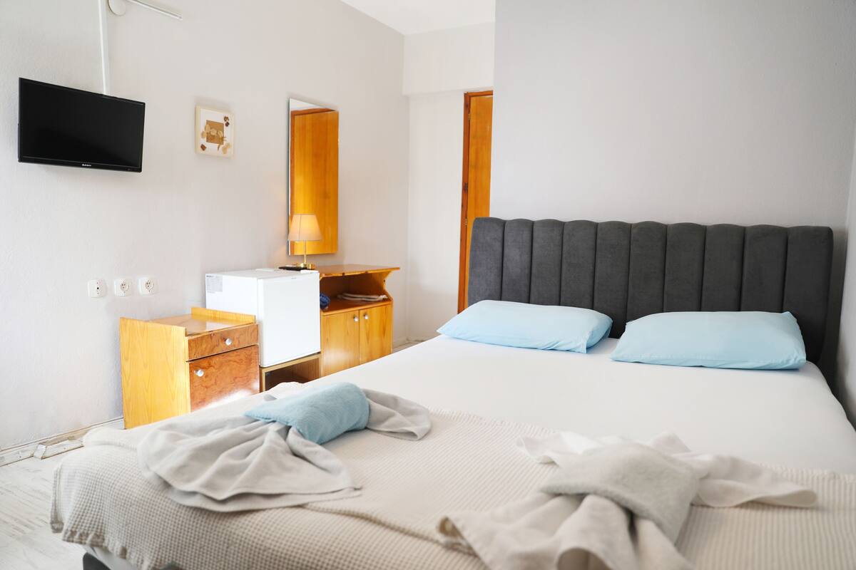 A hotel room with a bed, a TV, a wooden nightstand, a desk, and a mirror.