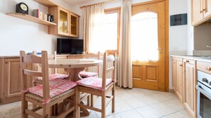 Una mesa de comedor de madera con sillas, un televisor y una cocina con armarios y estufa.