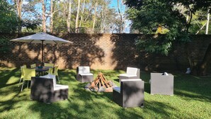 An outdoor patio with wicker furniture, a table, and chairs, surrounded by a brick wall and trees.
