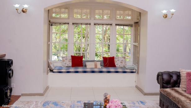 A room with a large arched window, a bench with cushions, a black leather sofa, and a small table with a vase.