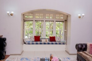 A room with a large arched window, a bench with cushions, a black leather sofa, and a small table with a vase. - The Vintage Manor (Blantyre)