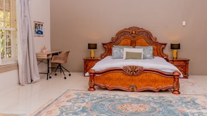 A bedroom with a large wooden bed, two bedside tables with lamps, a desk, and a chair.
