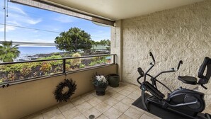 Un balcón con vista al océano, una bicicleta estática y una planta en maceta.