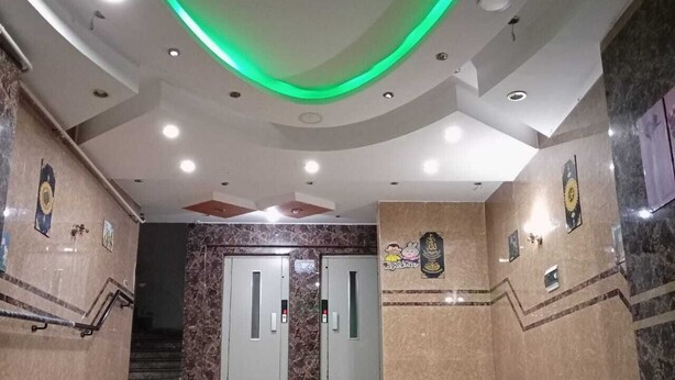 Un vestíbulo con paredes de mármol, una escalera y un techo iluminado en verde.