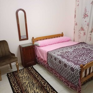 Une chambre à coucher avec un lit en bois, une table de chevet en bois, une chaise, un miroir et un tapis à motifs.