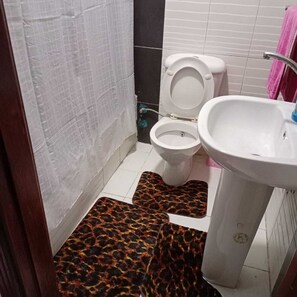 Une salle de bain avec des toilettes blanches, un lavabo blanc et un tapis à motifs léopard sur le sol.