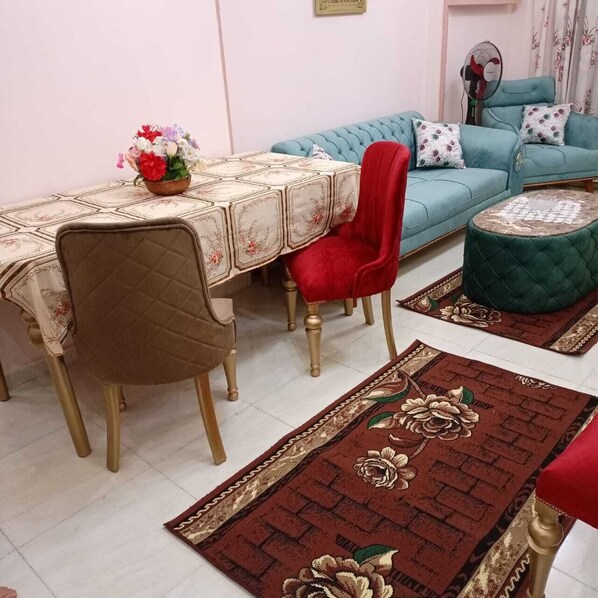 Un coin repas avec une table dressée pour quatre personnes, une chaise rouge, un canapé bleu et un pouf vert.