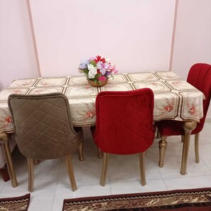 Une table à manger recouverte d’une nappe à motifs floraux, deux chaises avec un revêtement en tissu matelassé et un vase rempli de fleurs.