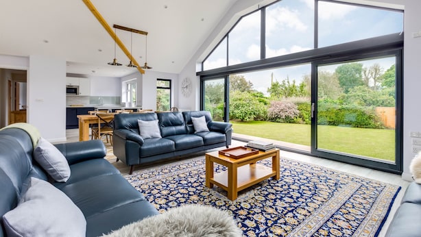 A spacious living room with a large black leather sofa, a wooden coffee table, and a patterned rug. - The Garden House (Wadebridge)