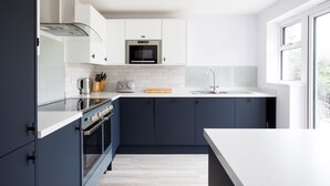 A modern kitchen with dark blue cabinets, a stainless steel oven, a microwave, and a white countertop. - The Garden House (Wadebridge)