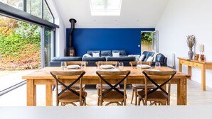 A modern dining area with a wooden table set for four, a blue accent wall, and a view of the outdoors. - The Garden House (Wadebridge)