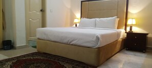 A neatly made bed with a beige headboard, two bedside lamps, and a red patterned rug. - Impeccable 3-bed Apartment in Lahore (Lahore)