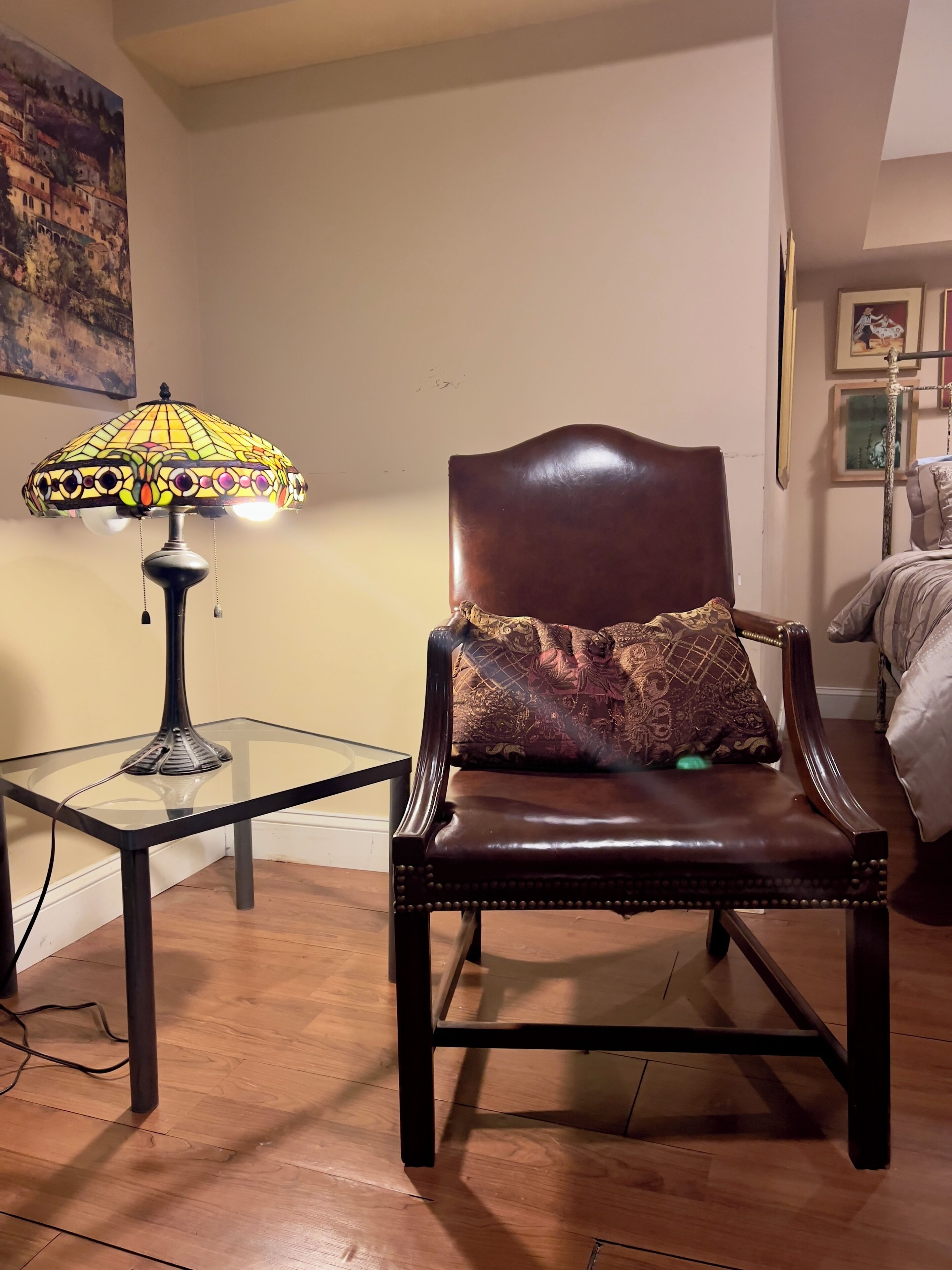 Une chaise avec un coussin à motifs, une table en verre avec une lampe et un tableau accroché au mur.