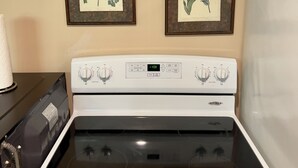 Uma cozinha com fogão branco, duas ilustrações botânicas emolduradas na parede e um dispensador de papel toalha.