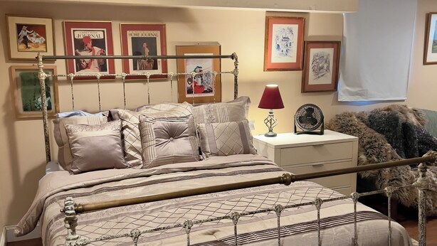 Quarto com cama, mesa de cabeceira com abajur e quadros na parede.