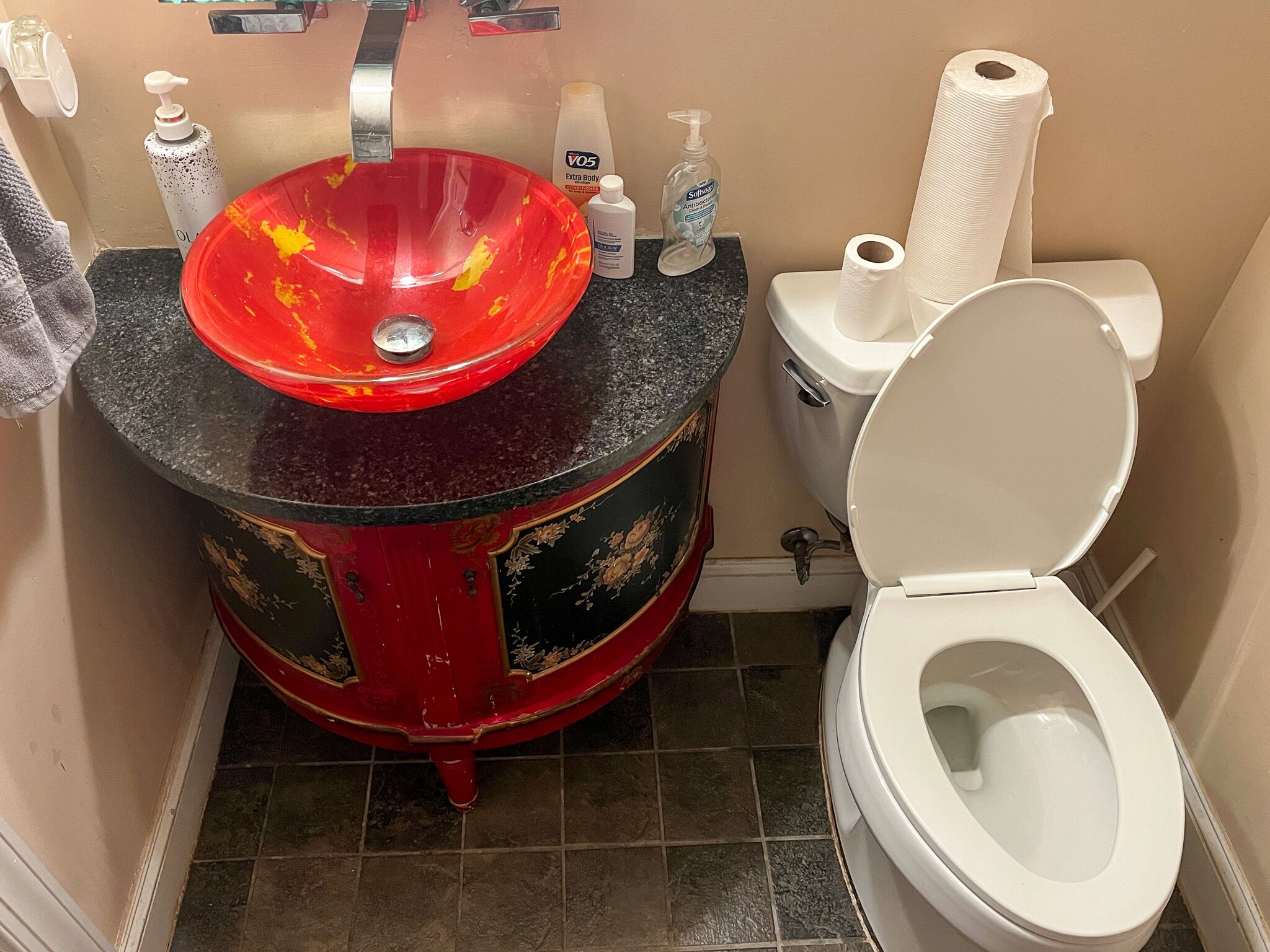 Une salle de bain avec un lavabo rouge, des toilettes et un plan de toilette noir.