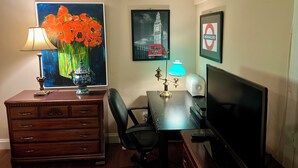 Um quarto com uma escrivaninha de madeira, uma cadeira, uma luminária, uma TV, uma cômoda e decoração nas paredes, incluindo uma pintura de flores, um ponto turístico de Londres e uma placa da linha de metrô de Londres.