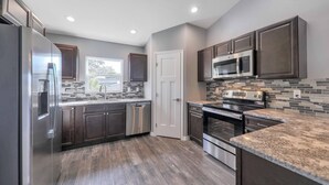 A modern kitchen with stainless steel appliances, dark wood cabinets, and a tiled backsplash. -  Lakefront Retreat w/ Dock, Kayaks & Sunset Views – Peaceful Escape! (Lake Placid)